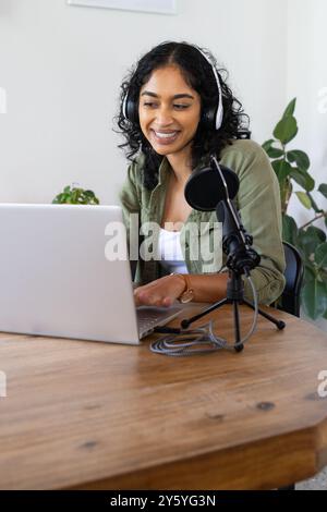 Mit Laptop und Mikrofon, lächelnde Frau während der Aufnahme von Podcasts zu Hause, Kopierraum Stockfoto