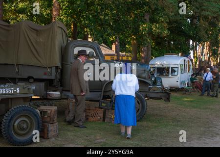 Holt, Norfolk, Vereinigtes Königreich – 21. SEPTEMBER 2024: Mann und Frau in Zivilkleidung der 1940er Jahre neben einem Militärfahrzeug Stockfoto