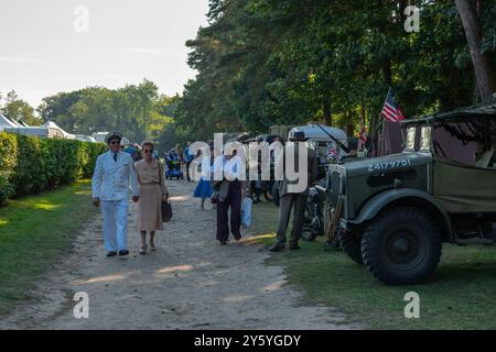 Holt, Norfolk, Vereinigtes Königreich - 21. SEPTEMBER 2024: Menschen, die in Vintage-Kleidung der 1940er Jahre gekleidet sind, gehen an einem Militärwagen vorbei Stockfoto