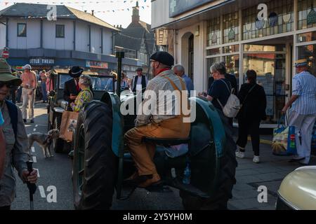 Sheringham, Norfolk, Vereinigtes Königreich - 21. SEPTEMBER 2024: Bauer in Uniform sitzt am Wochenende der 1940er Jahre auf einem alten Traktor auf der Straße Stockfoto