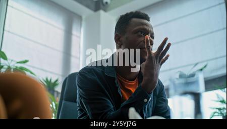 Wütender Afroamerikaner verliert seine Beherrschung, beginnt zu kämpfen und ruft während der Paartherapie. Multiethnisches junges Ehepaar mit Konflikt bei der Beratung mit Familienpsychologen. Scheidungsprozess. Stockfoto
