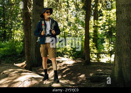 Selbstbewusster Senior Tourist, der mit Rucksack im Wald steht und wegblickt Stockfoto