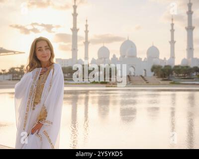 Reisen Sie in die Vereinigten Arabischen Emirate, Abu Dhabi. Frau in weißem arabischem Kleid, die Sheikh Zayed große weiße Moschee ansieht. Berühmte Besichtigungstour in Abu Dhabi. Stockfoto