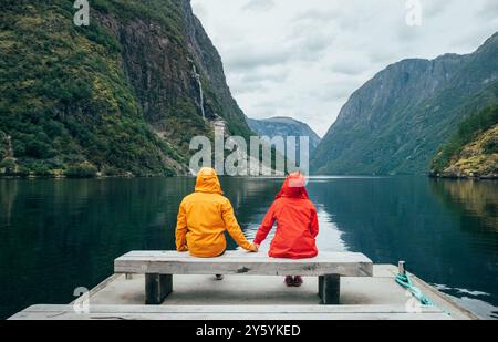 Glückliches Paar in hellen, winddichten Jacken auf der Bank auf der norwegischen Nærøyfjord Bank in Gudvangen, Norwegen. Reisen, Schönheit Stockfoto