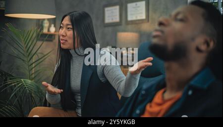Wütende asiatische Freundin beginnt zu kämpfen, ruft den Freund an. Aggressiver Afroamerikaner verliert die Beherrschung, schreit zurück. Multiethnische junge Familie mit Konflikten während der Beratung mit Psychotherapeuten. Stockfoto