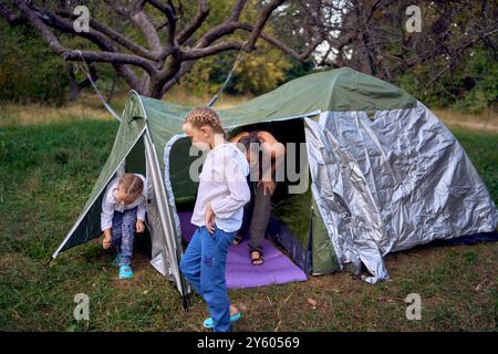 Mutter und kleine Töchter bauen im Wald ein Touristenzelt auf und campen mit Kindern Stockfoto