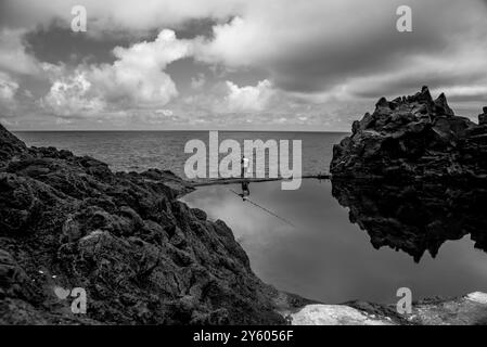 fischer mit gelber Weste und Angelrute in den sanften Klippen der natürlichen Pools im Norden von Madeira Portugal Stockfoto