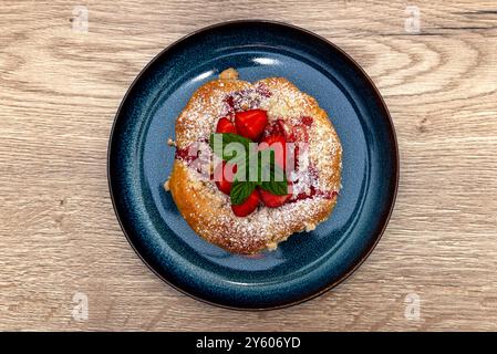 Handgemachter Hefekuchen mit Erdbeeren und Pudding, auf einem blauen Teller liegend. Stockfoto