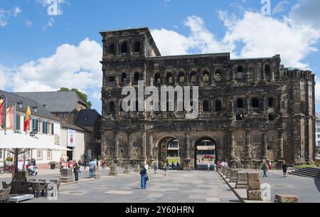 Ein großes, altes Gebäude mit mehreren Bögen und Fenstern, umgeben von Menschen auf einer sonnigen Straße, Porta Nigra, Schwarzes Tor, römisches Stadttor, Trier, Rechts Stockfoto