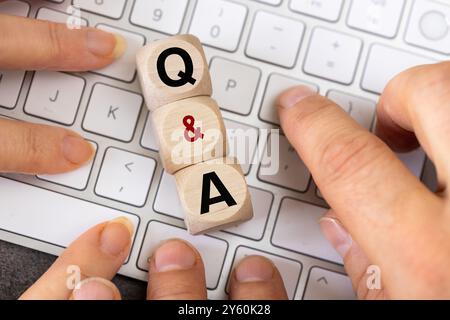 Q&A-Symbol. Fragen und Antworten, konzeptuelle Wörter auf Holzwürfeln, viele Hände auf der weißen Computertastatur, die Antworten auf Fragen suchen Stockfoto