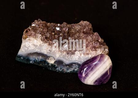 Kristalle einer Amethyst-Geode zusammen mit einem polierten Amethyst-Tumble-Stein auf schwarzem Hintergrund Stockfoto