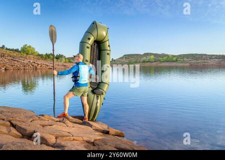 Senior männlicher Paddler startet ein aufblasbares Packboot an einem Ufer des Horsetooth Reservoir in Colorado Stockfoto