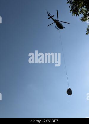 Ein Hubschrauber, der ein Paket in den Bergen des Comer Sees transportiert Stockfoto