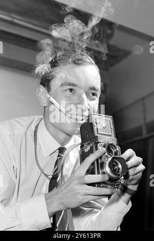 Mit dem Kopf in Zigarettenrauch verkrankt, kann der Gesellschaftsfotograf Tom Hustler mit seiner Kamera in seinem Studio in Belgravia arbeiten. Der alte etonische Tom, 26 Jahre alt, soll der nächste königliche Fotograf werden, der Tolny Armstrong-Jones ersetzen wird, der die Schwester der Königin Pricncess Margaret heiratete. Tom hat bereits Fotos von Prinz Charles und Prinzessin Anne gemacht, sowie die offiziellen Gruppenfotos von der Hochzeit der Tochter von Earl Mountbatten. Erst vor drei Jahren war er Sachbearbeiter an der Börse 12. August 1960TOM HUSTLER - NEXT ROYAL PHOTOGRAPHER / 12. AUGUST 1960 Stockfoto