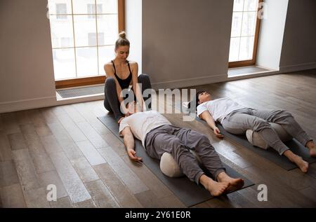 Junge weibliche Yogalehrerin führt Meditation Dehnkurs kleine Gruppe Leute Zimmer große Fenster Stockfoto