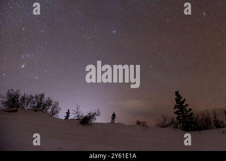 Nacht in der Carcross-Wüste, Yukon-Territorium mit glitzernden Nachthimmel-Sternen und Personen-Silhouette auf einem Berggipfel. Stockfoto