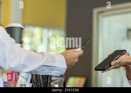 Eine Frau nutzt eine App auf ihrem Smartphone, um Kaffee am Coffee Shop-Schalter zu scannen und zu bezahlen, weil es bequem ist.Concept Scan, um Waren zu bezahlen Stockfoto