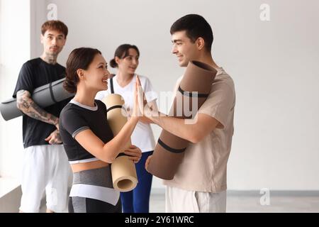 Sportliche Jugendliche mit Yogamatten, die sich gegenseitig High-Five im Fitnessstudio geben Stockfoto