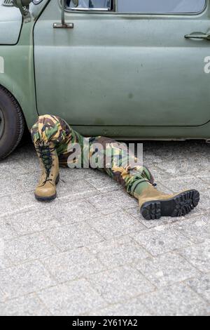 Militärmechaniker in Tarnung, der unter einem alten Fahrzeug arbeitet. Die Szene erfasst das Wesen der Wartung und Reparatur vor Ort in einem realistischen Outdo Stockfoto