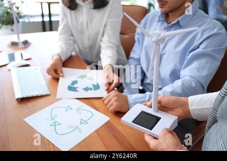 Ingenieure mit Windkraftanlagenmodell und Recycling-Schildern im Büro, Nahaufnahme Stockfoto