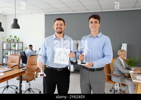 Männliche Ingenieure mit Windturbinenmodellen und Recycling-Schild im Büro Stockfoto