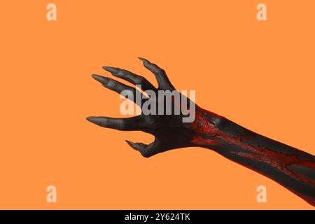 Schwarze Hexenhand mit Klauen auf orangem Hintergrund. Halloween-Feier Stockfoto