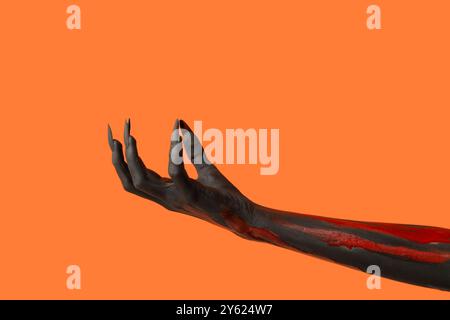 Schwarze Hexenhand mit Klauen auf orangem Hintergrund. Halloween-Feier Stockfoto