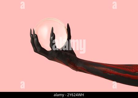 Schwarze Hexenhand mit Krallen und Kristall auf rosa Hintergrund. Halloween-Feier Stockfoto