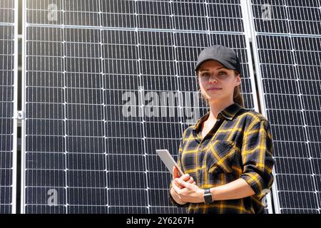 Porträt einer Technikerin mit einem digitalen Tablet, die selbstbewusst vor großen Solarpaneelen steht. Stockfoto