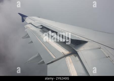 Nahaufnahme eines Flugzeugflügels mit verlängerten Laschen in dichtem Nebel, Flugverkehr über den Wolken. Stockfoto