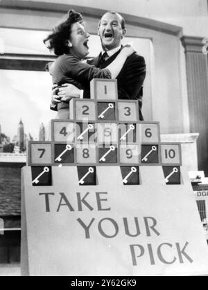 London : Frau Janice Isaacs von Elms Lane, Wembley, wird von Michael Miles, dem Kommandeur der ITV-Sendung " Take Your Pick ", beglückwünscht, nachdem er ihr gesagt hat, dass sie einen Rolling Pin in der Sendung gewonnen hat - plus eine gute Chance auf eine Rückfahrt für sich und ihren Mann nach Amerika. Herr Isaacs ist darauf angewiesen, dass die Zuschauer in den nächsten drei Wochen korrekte Antworten auf Hinweise geben, die die Verstecke von Abschnitten des Tickets angeben, wenn sie gewinnen will.31. Dezember 1955 Stockfoto