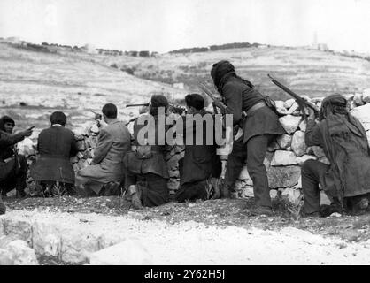 Foto auf dem Ölberg mit Blick auf Jerusalem, als Araber hinter einer Steinmauer nach jüdischen Scharfschützen aus der Altstadt Jerusalems, die jetzt von der Arabischen Legion gefangen genommen wurde, beobachteten. Die Araber bereiten sich nun auf einen Angriff auf das Labyrinth aus Straßen und Steinbauten in den neuen Gebieten Jerusalems vor. Fotoshows; Araber mit Gewehren halten Ausschau nach Scharfschützen vom Ölberg in der Gegend der Hebräischen Universität. 31. Mai 1948 Stockfoto