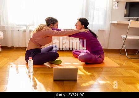 Online-Workout. Schöne Frau und ihr Teenager Mädchen, die die Übung machen und Yoga zu Hause üben, sitzen in Lotusposition auf Yogamatte. Gut gelaunt Stockfoto