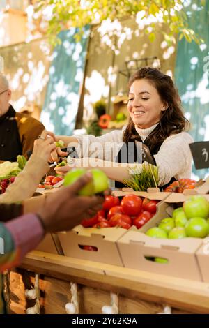 Verschiedene Personen erhalten Obstproben auf dem Bauernmarkt, stöbern auf frisch geerntetem Obst und Gemüse auf dem lokalen Bauernmarkt. Lächelnder Anbieter, der seinen Kunden Apfelscheiben zur Verkostung schenkt. Stockfoto