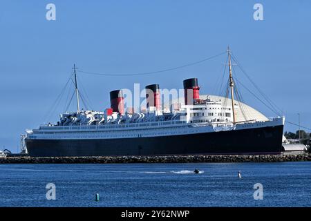 LONG BEACH, KALIFORNIEN - 19. SEPTEMBER 2024: The Queen Mary Hotel. Permanent im Hafen verankert, während ein Jet-Ski vorbeizieht. Stockfoto