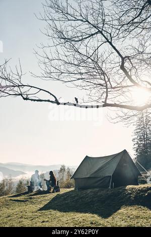 Frische Luft und perfekte Aussicht. Ein junges Paar, das morgens Kaffee trinkt, während es in der Nähe des Zeltes in den Bergen sitzt Stockfoto