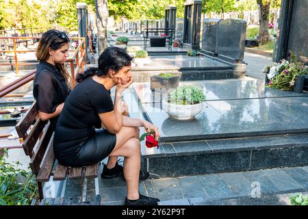 Mutter und Tochter in Trauer, in schwarzer Kleidung, mit einer Blume und Trauer um einen verstorbenen geliebten Menschen auf dem Friedhof Stockfoto