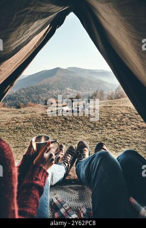 Die beste Reise aller Zeiten. Nahaufnahme eines jungen Paares beim Morgenkaffee, während sie den Blick auf die Bergkette von ihrem Zelt aus genießen Stockfoto