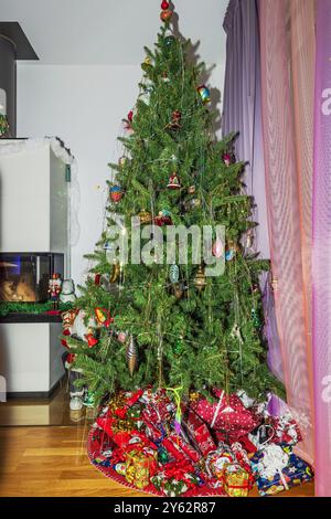 Wunderschön dekorierter Weihnachtsbaum mit farbenfrohen Ornamenten und präsentiert sich darunter in einer gemütlichen Atmosphäre. Stockfoto