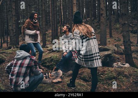 Leben voller Freundschaft. Gruppe glücklicher junger Leute, die am Lagerfeuer stehen, während sie im Wald wandern Stockfoto