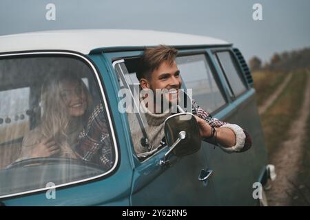 Der beste Weg, um der Stadt zu entkommen. Hübscher junger Mann, der sich aus dem Fenster des Van lehnte und lächelte, während er mit auf den Beifahrersitzen saß Stockfoto