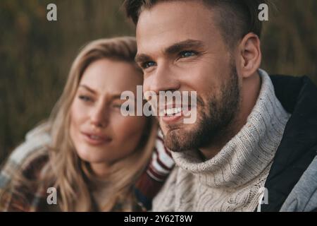 Keine Sorge. Wunderschönes junges Paar, das wegschaut und lächelt, während es draußen auf dem Feld sitzt Stockfoto