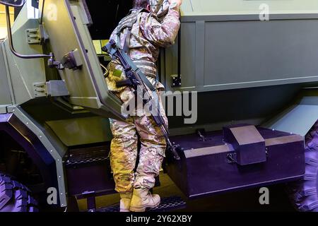 Soldat in Tarnuniform mit einem Sturmgewehr in der Nähe eines gepanzerten Autos. Militärische Ausbildung Stockfoto