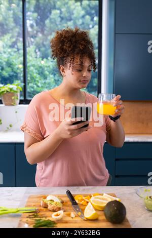 Smartphone halten und Orangensaft trinken, Frau in der Küche, zu Hause, zu Hause Stockfoto