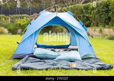 Camping im Hinterhof, blaues Zelt mit Schlafsäcken und Kissen auf Gras Stockfoto