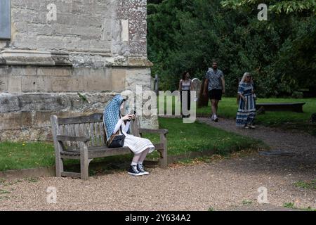 Stratford Upon Avon - Vereinigtes Königreich; 28. Juli 2024; Junge Frau mit blauem gemustertem Schleier über dem Kopf, der vor der Sonne geschützt ist und auf einer Sitzbank sitzt Stockfoto