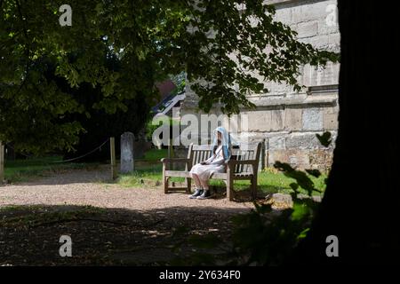 Stratford Upon Avon - Vereinigtes Königreich; 28. Juli 2024; Junge Frau mit blauem gemustertem Schleier über dem Kopf, der vor der Sonne geschützt ist und auf einer Sitzbank sitzt Stockfoto