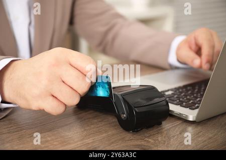 Mann, der über Terminal bezahlt, während er einen Laptop am Holztisch benutzt, Nahaufnahme Stockfoto