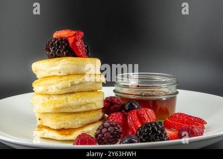 Leckere vegane, vegetarische Butter milchfreie Pfannkuchen mit Beeren belegt, Ahornsirup auf weißem Teller mit schwarzem Hintergrund. Stockfoto