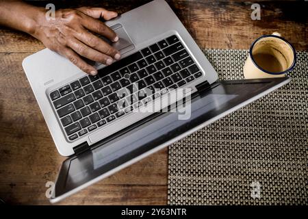 Mann, der zu Hause an einem Laptop arbeitet, begleitet von einer Tasse Kaffee Stockfoto